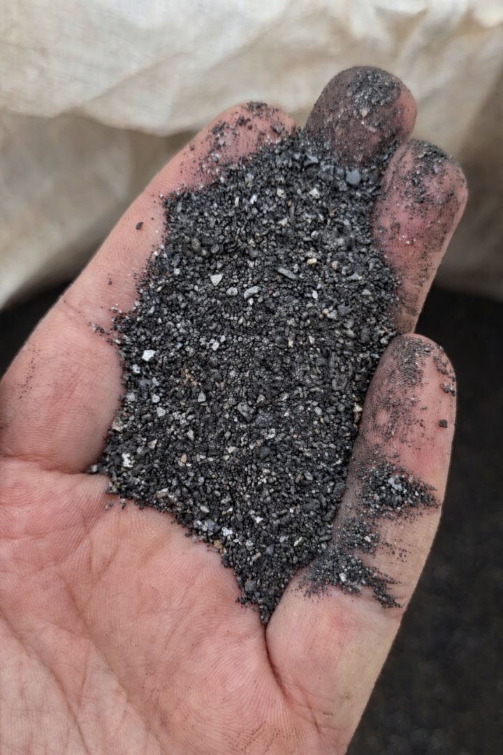 Handful of dark grey fluorspar flotation concentrate taken from a jumbo bag